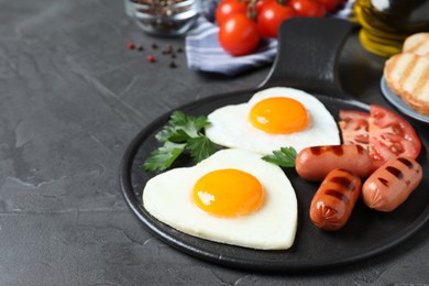 Photo of Delicious breakfast with heart shaped fried eggs and sausages on dark grey table