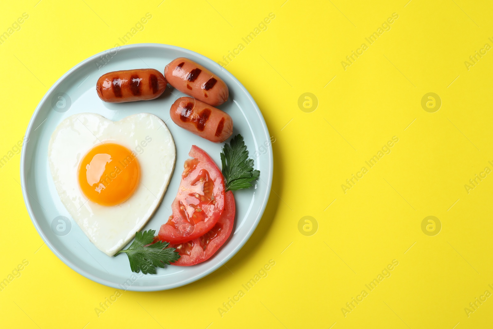 Photo of Plate of heart shaped fried egg and sausages on yellow background, top view. Space for text