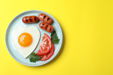 Photo of Plate of heart shaped fried egg and sausages on yellow background, top view. Space for text