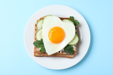 Photo of Plate of tasty sandwich with heart shaped fried egg on light blue background, top view