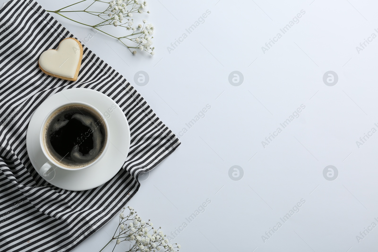 Photo of Cup of coffee, heart shaped cookie, napkin and flowers on white background, top view