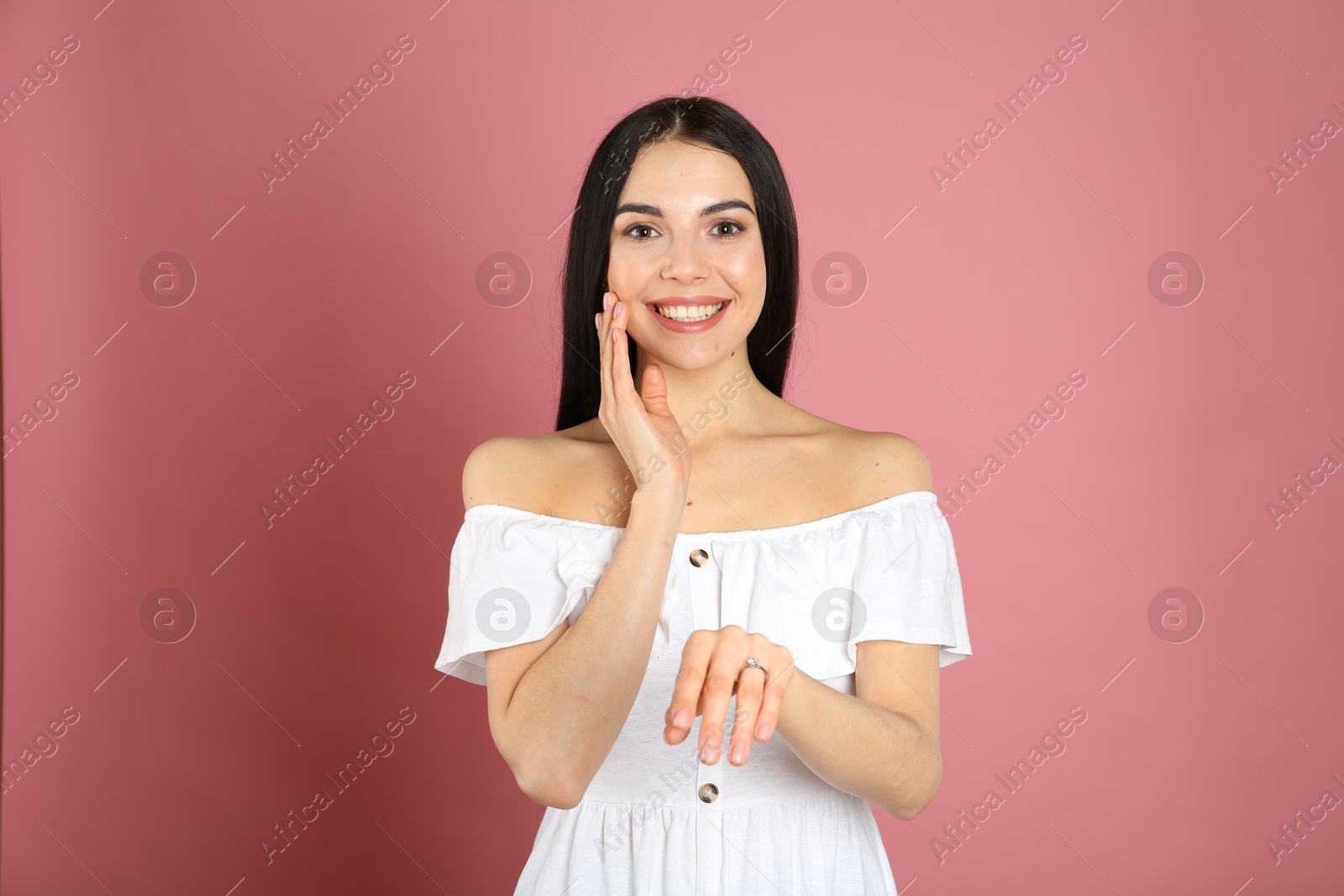 Photo of Happy young woman wearing beautiful engagement ring on pink background