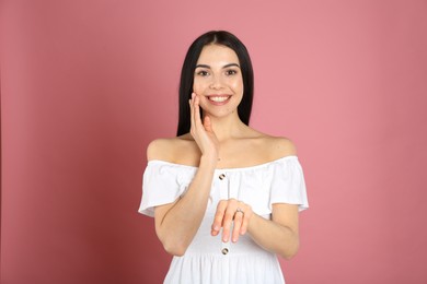 Happy young woman wearing beautiful engagement ring on pink background