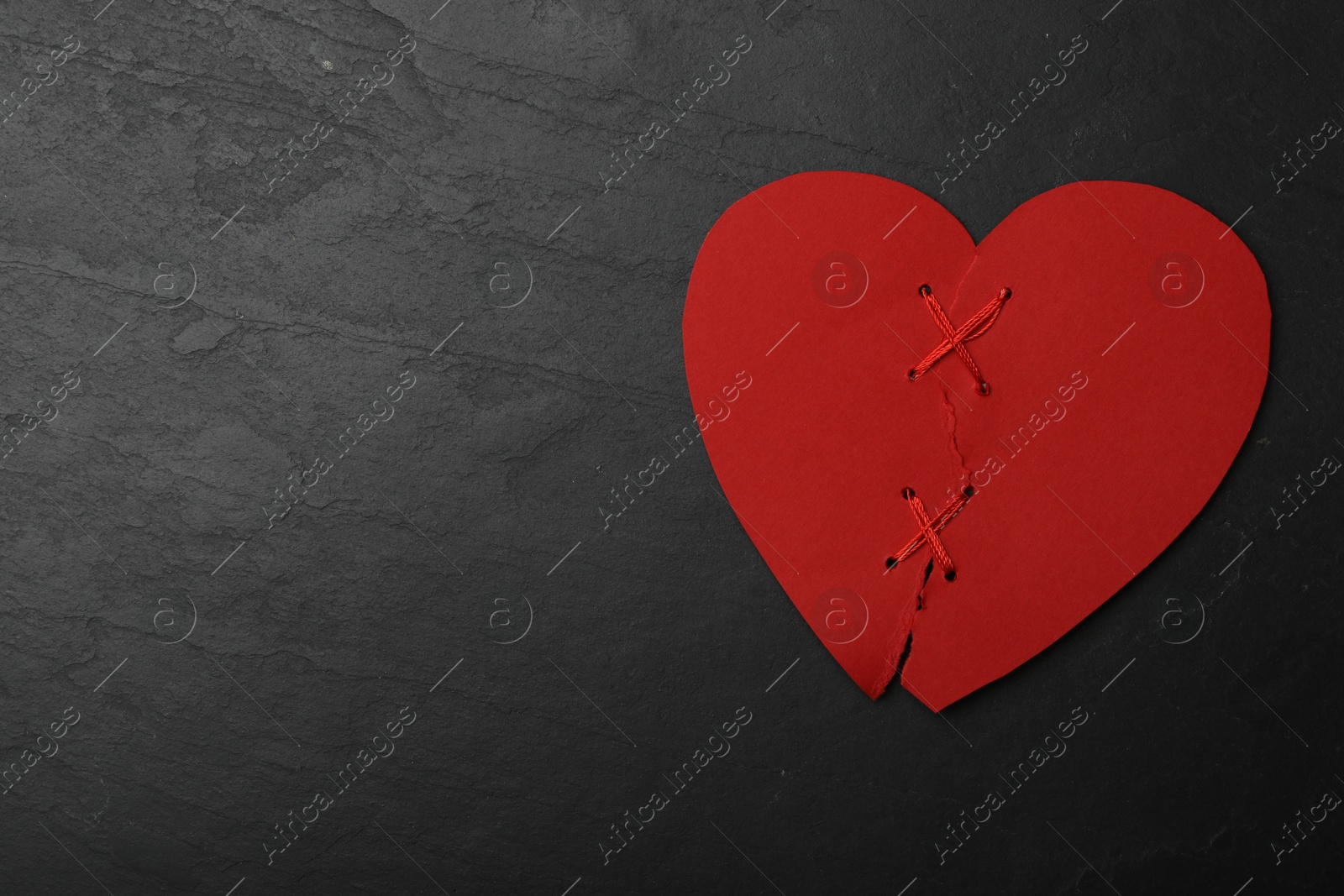 Photo of Top view of torn paper heart sewed with thread on black stone background, space for text. Relationship problems concept