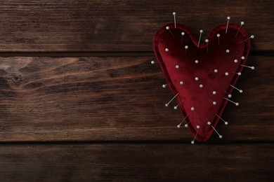 Photo of Top view of heart shaped cushion with sewing pins on wooden background, space for text. Relationship problems concept