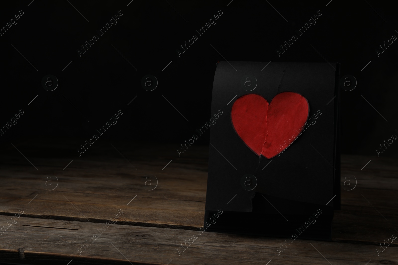 Photo of Torn black sheet with heart sticker on wooden table, space for text. Relationship problems concept