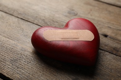 Photo of Heart with medical patch on wooden table, closeup. Relationship problems concept