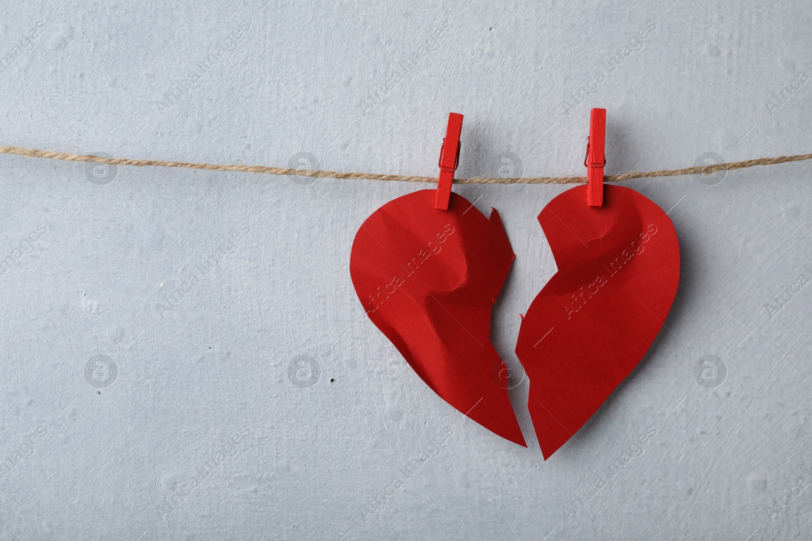 Photo of Halves of torn paper heart pinned on laundry string near light wall, space for text. Relationship problems concept