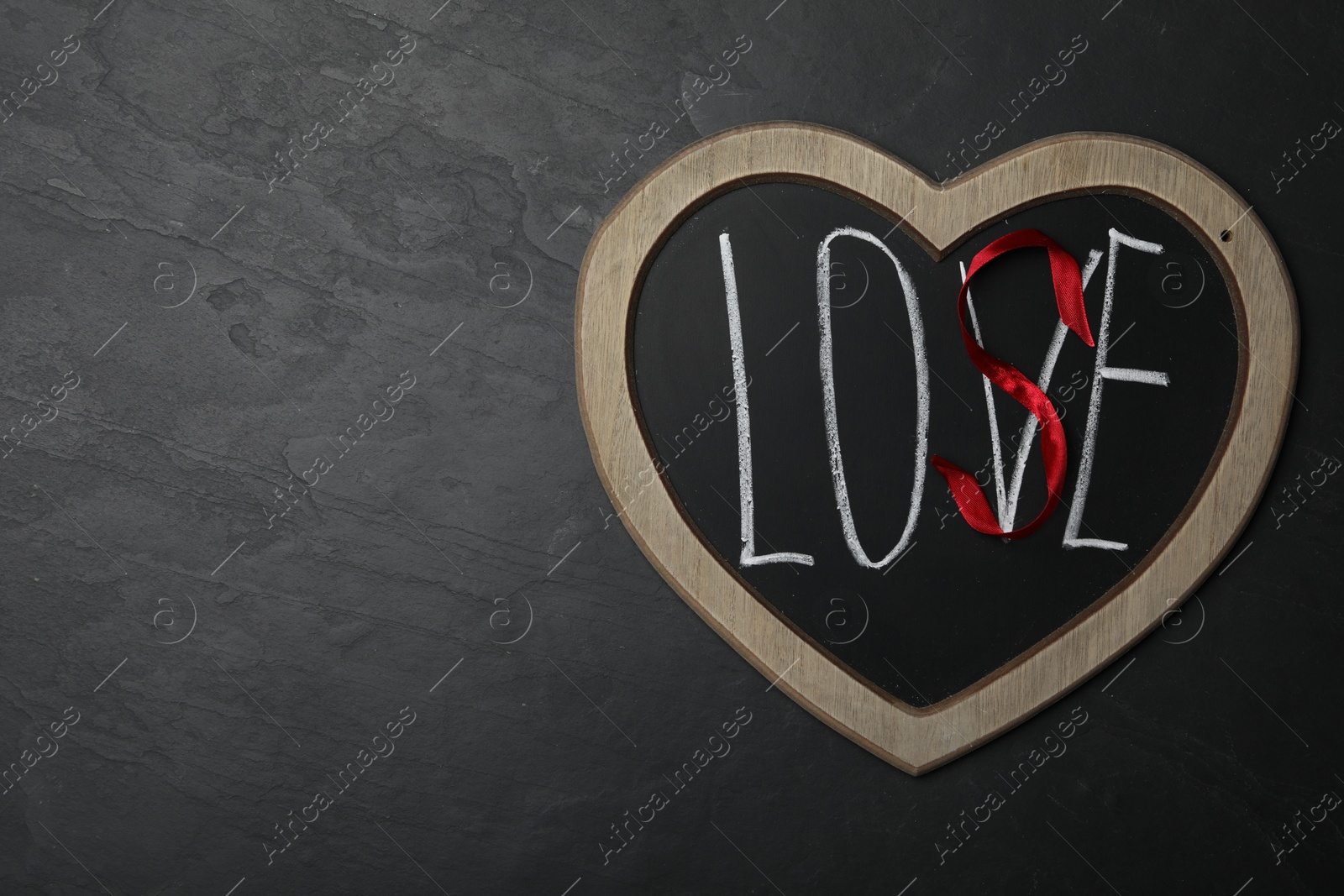 Photo of Heart shaped blackboard with word LOVE and letter S of red ribbon on dark background, top view. Composition symbolizing problems in relationship