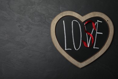 Photo of Heart shaped blackboard with word LOVE and letter S of red ribbon on dark background, top view. Composition symbolizing problems in relationship