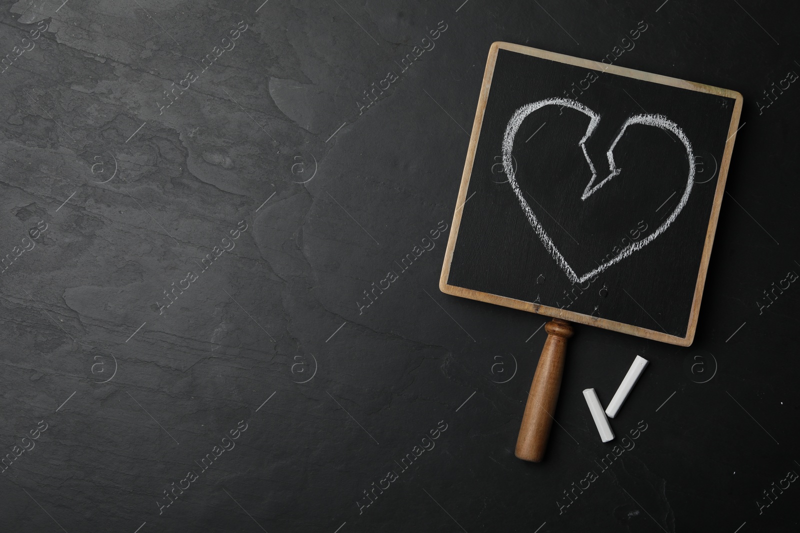 Photo of Blackboard with drawn broken heart and pieces of chalk on dark background, flat lay. Relationship problems concept