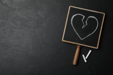 Blackboard with drawn broken heart and pieces of chalk on dark background, flat lay. Relationship problems concept