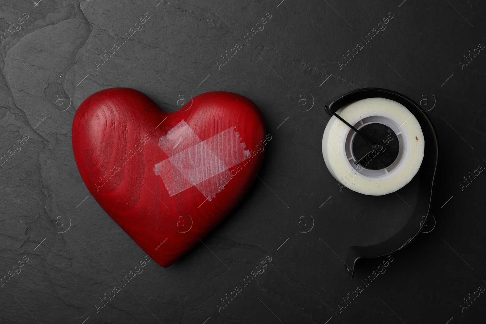 Photo of Red wooden heart and adhesive tape on black stone background, flat lay. Relationship problems concept