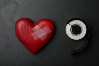 Photo of Red wooden heart and adhesive tape on black stone background, flat lay. Relationship problems concept