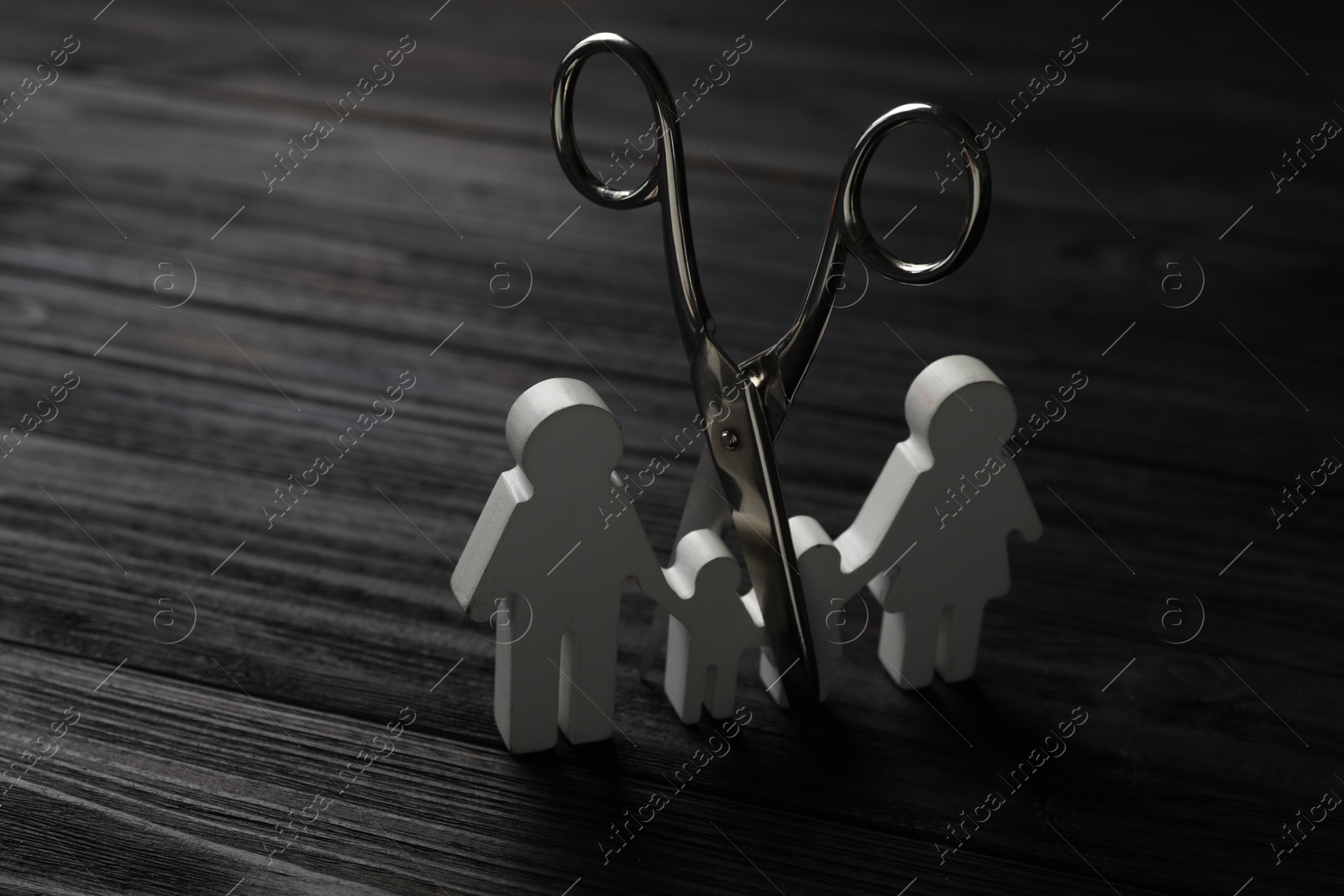 Photo of Family figure and scissors on black wooden table. Relationship problems concept