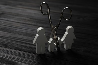 Photo of Family figure and scissors on black wooden table. Relationship problems concept