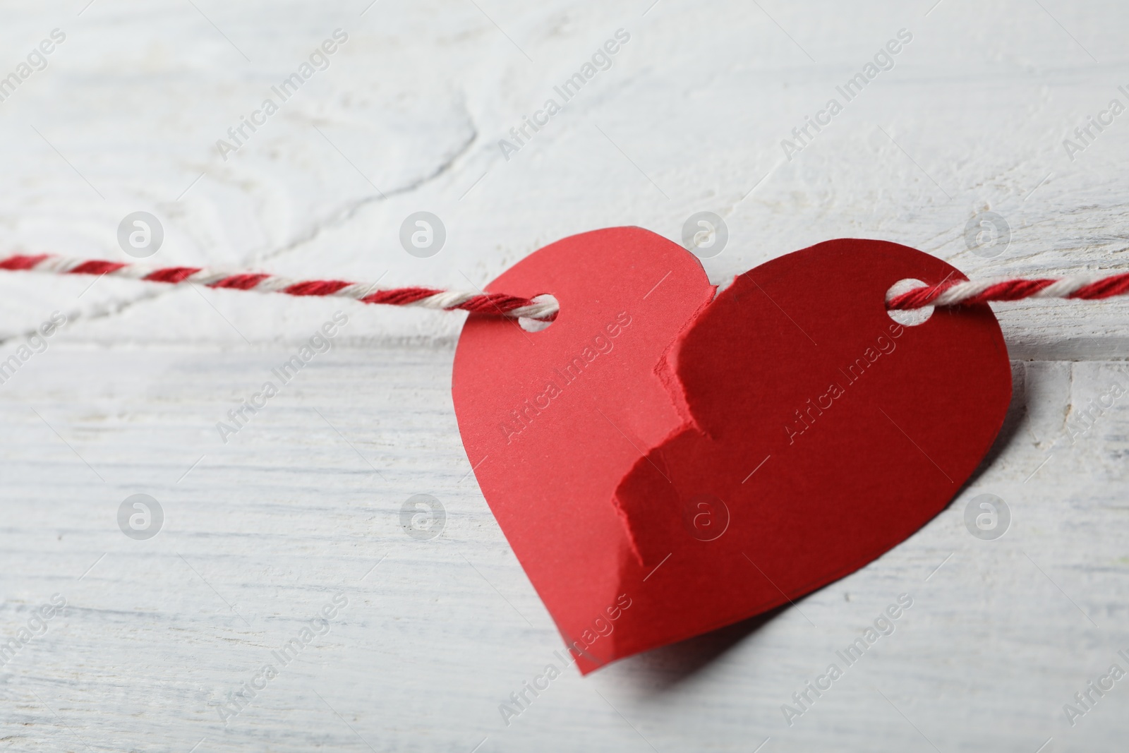 Photo of Broken red paper heart and rope on white wooden table, closeup. Relationship problems concept