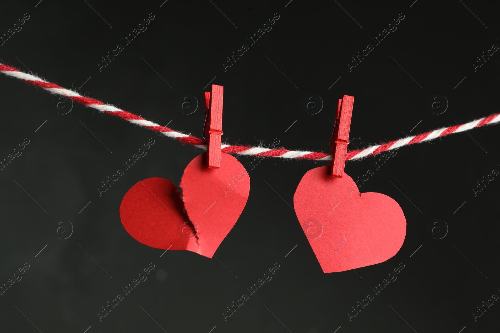 Photo of Broken and whole red paper hearts on rope against black background. Relationship problems concept