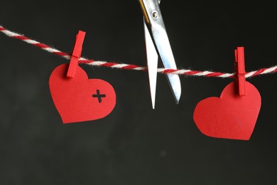 Photo of Red paper hearts on rope and scissors against black background. Composition symbolizing problems in relationship