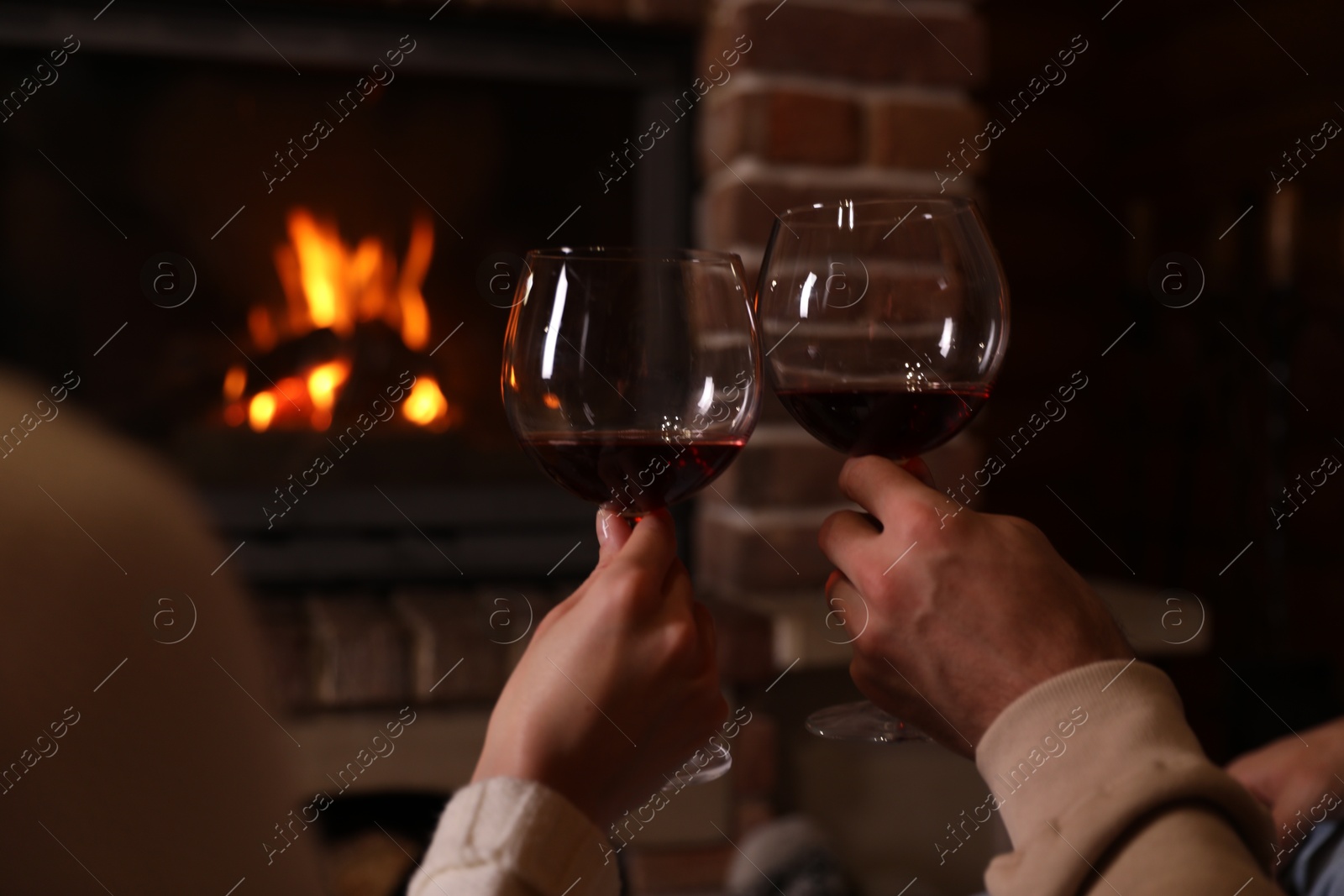 Photo of Couple with glasses of red wine near burning fireplace, closeup