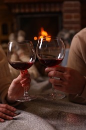 Photo of Couple with glasses of red wine near burning fireplace, closeup