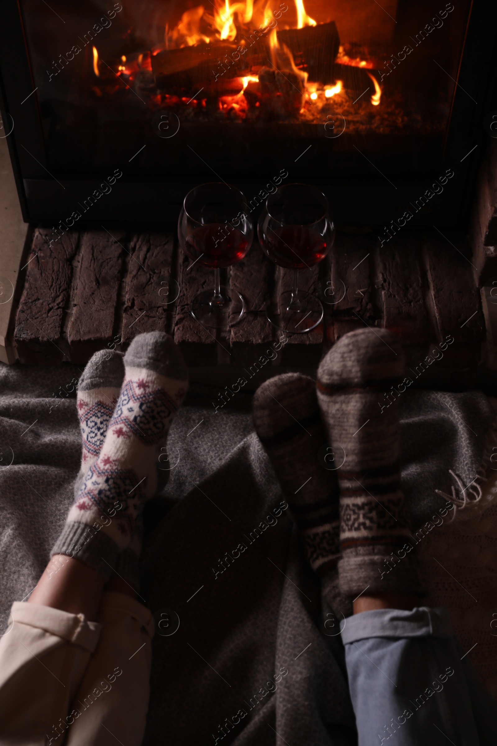 Photo of Couple and glasses of red wine near burning fireplace, closeup