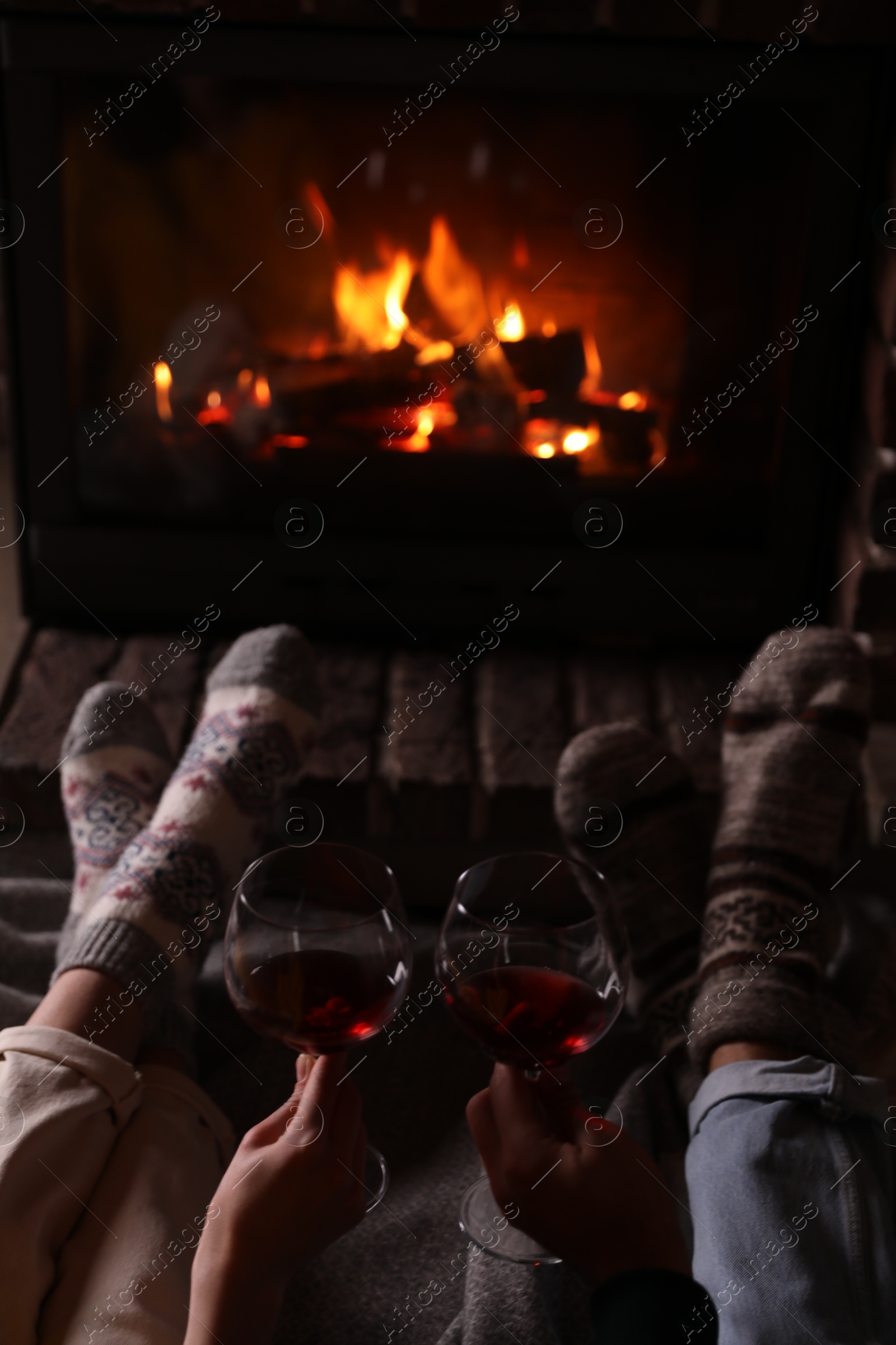 Photo of Couple with glasses of red wine near burning fireplace, closeup