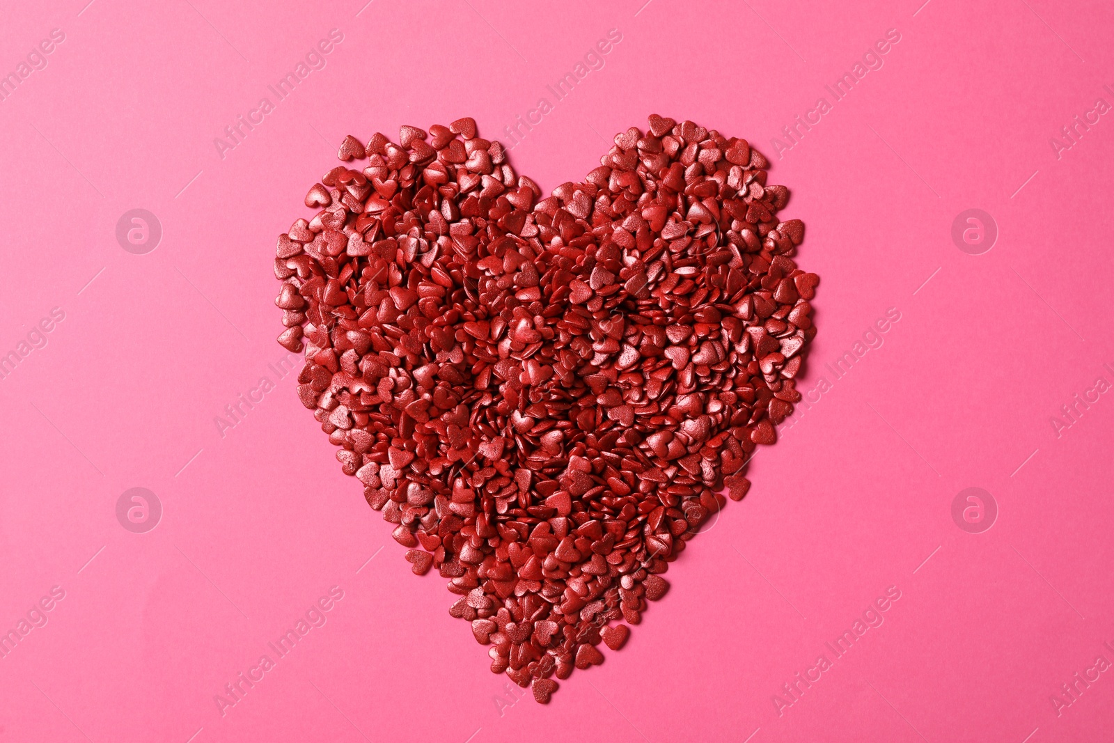 Photo of Heart made with red sprinkles on pink background, top view