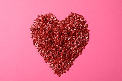 Photo of Heart made with red sprinkles on pink background, top view