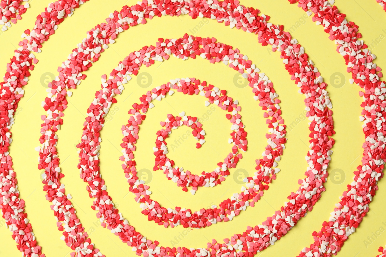 Photo of Spiral made of bright heart shaped sprinkles on yellow background, flat lay