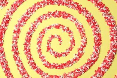 Photo of Spiral made of bright heart shaped sprinkles on yellow background, flat lay