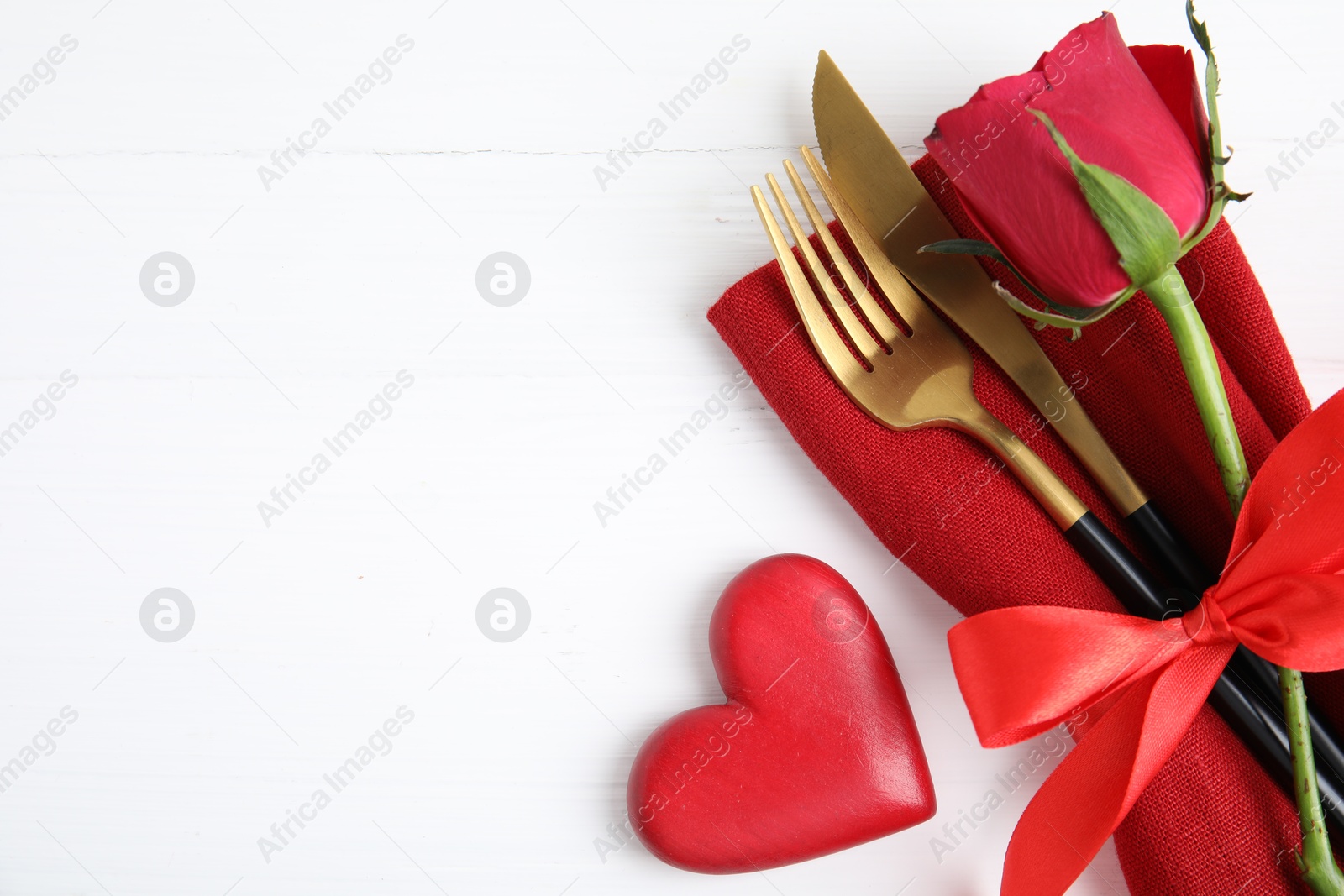 Photo of Top view of cutlery with napkin and decorative heart on white wooden table, space for text. Valentine's Day romantic dinner