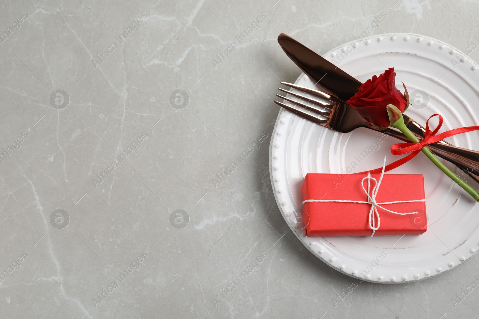 Photo of Beautiful place setting with gift box on light grey table, top view and space for text. Valentine's day romantic dinner