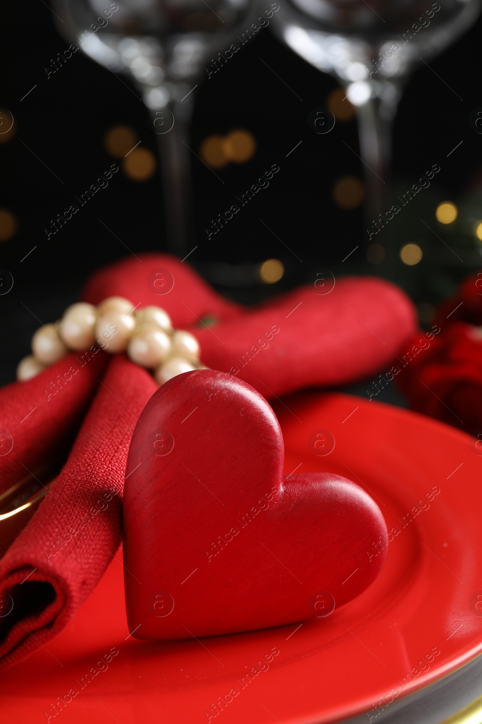 Photo of Beautiful place setting for romantic dinner on table against black background with blurred lights, closeup. Valentine's day celebration