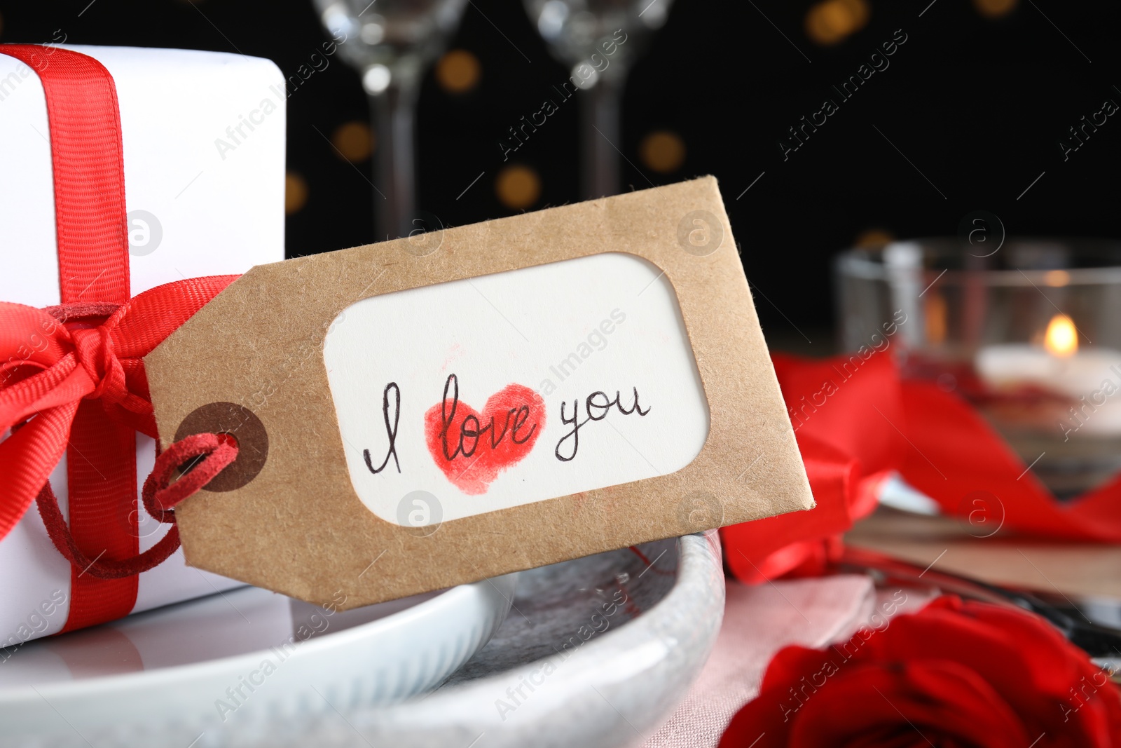 Photo of Beautiful place setting and tag with phrase I Love You on table against blurred lights, closeup. Valentine's day romantic dinner