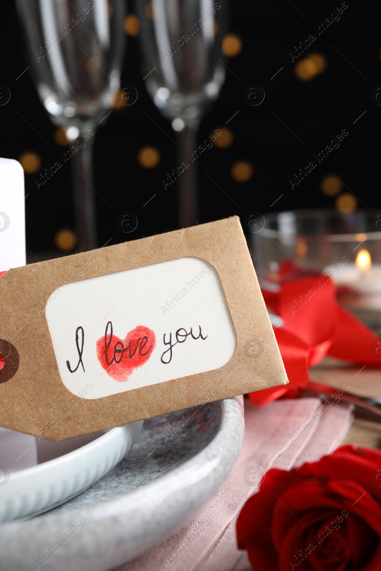 Photo of Beautiful place setting and tag with phrase I Love You on table against blurred lights, closeup. Valentine's day romantic dinner