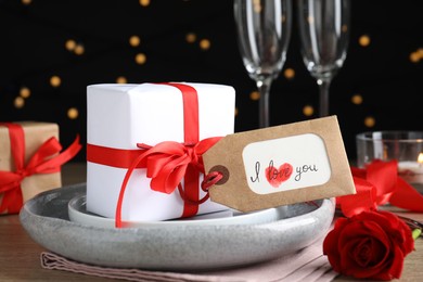 Photo of Beautiful place setting and tag with phrase I Love You on table against blurred lights, closeup. Valentine's day romantic dinner