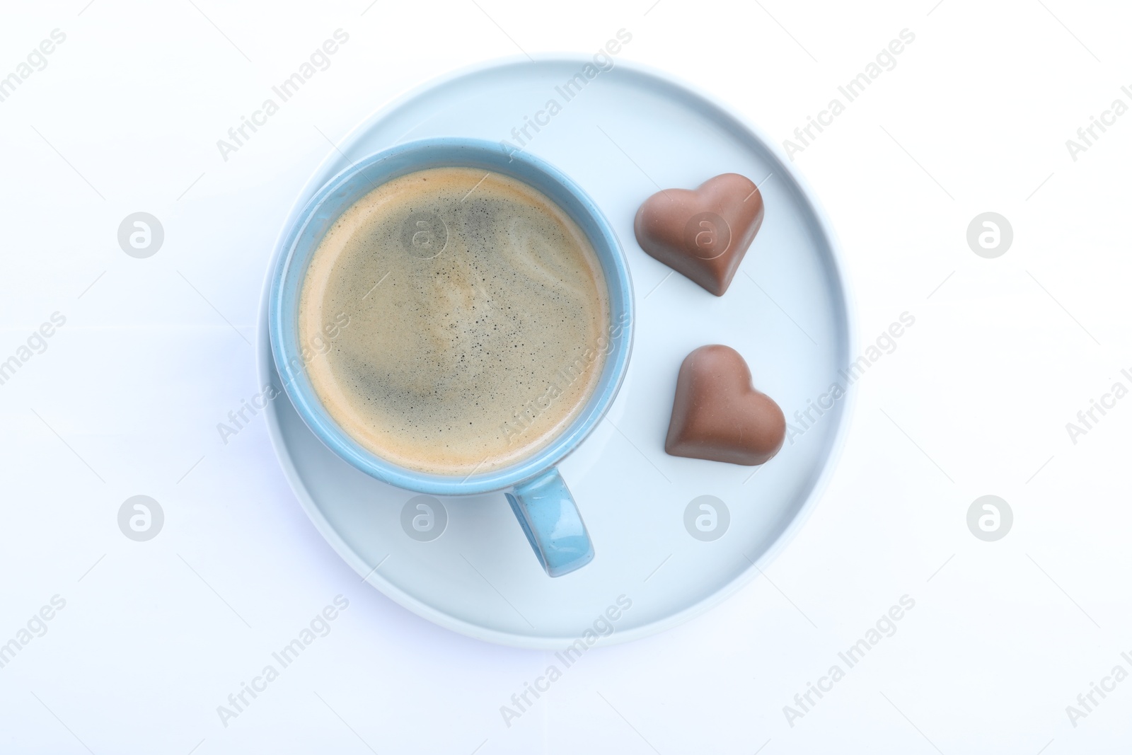 Photo of Romantic breakfast with cup of coffee and chocolate candies isolated on white, top view. Valentine's day celebration