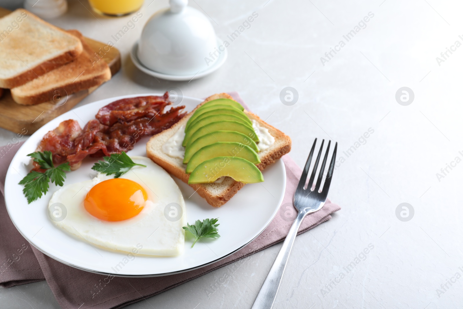 Photo of Romantic breakfast with fried bacon, heart shaped egg and avocado toast on light grey table. Valentine's day celebration