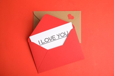 Photo of Card with phrase I Love You in envelope and paper heart on red background, flat lay