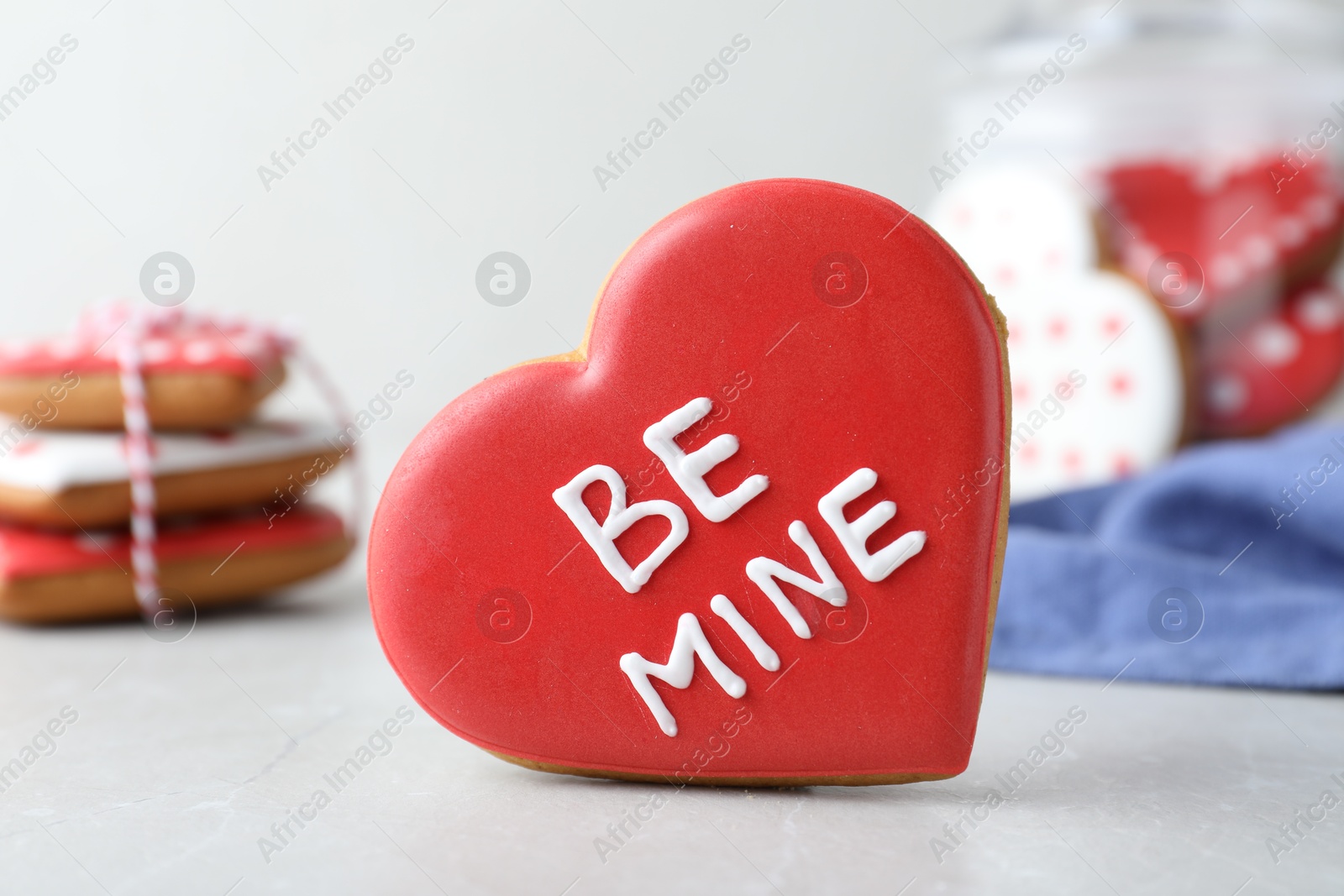 Photo of Delicious heart shaped cookie with phrase Be Mine on light table, closeup. Valentine's Day