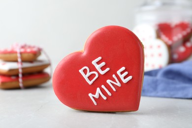 Photo of Delicious heart shaped cookie with phrase Be Mine on light table, closeup. Valentine's Day