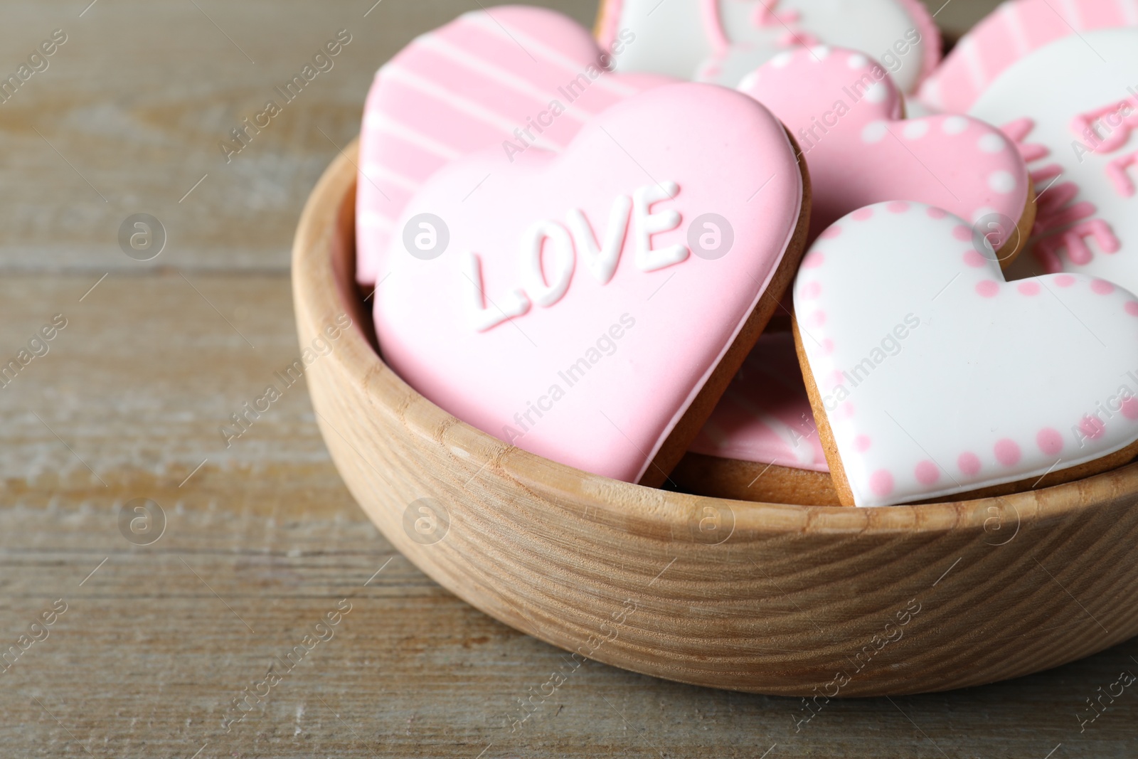 Photo of Valentine's day cookies in bowl on wooden table, closeup