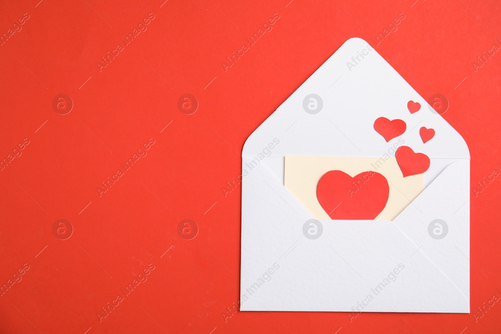 Photo of Envelope, card and paper hearts on red background, top view with space for text. Love letter