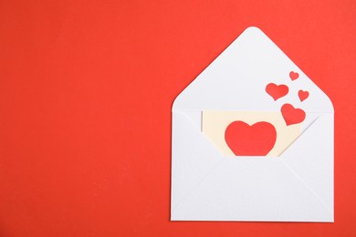 Photo of Envelope, card and paper hearts on red background, top view with space for text. Love letter