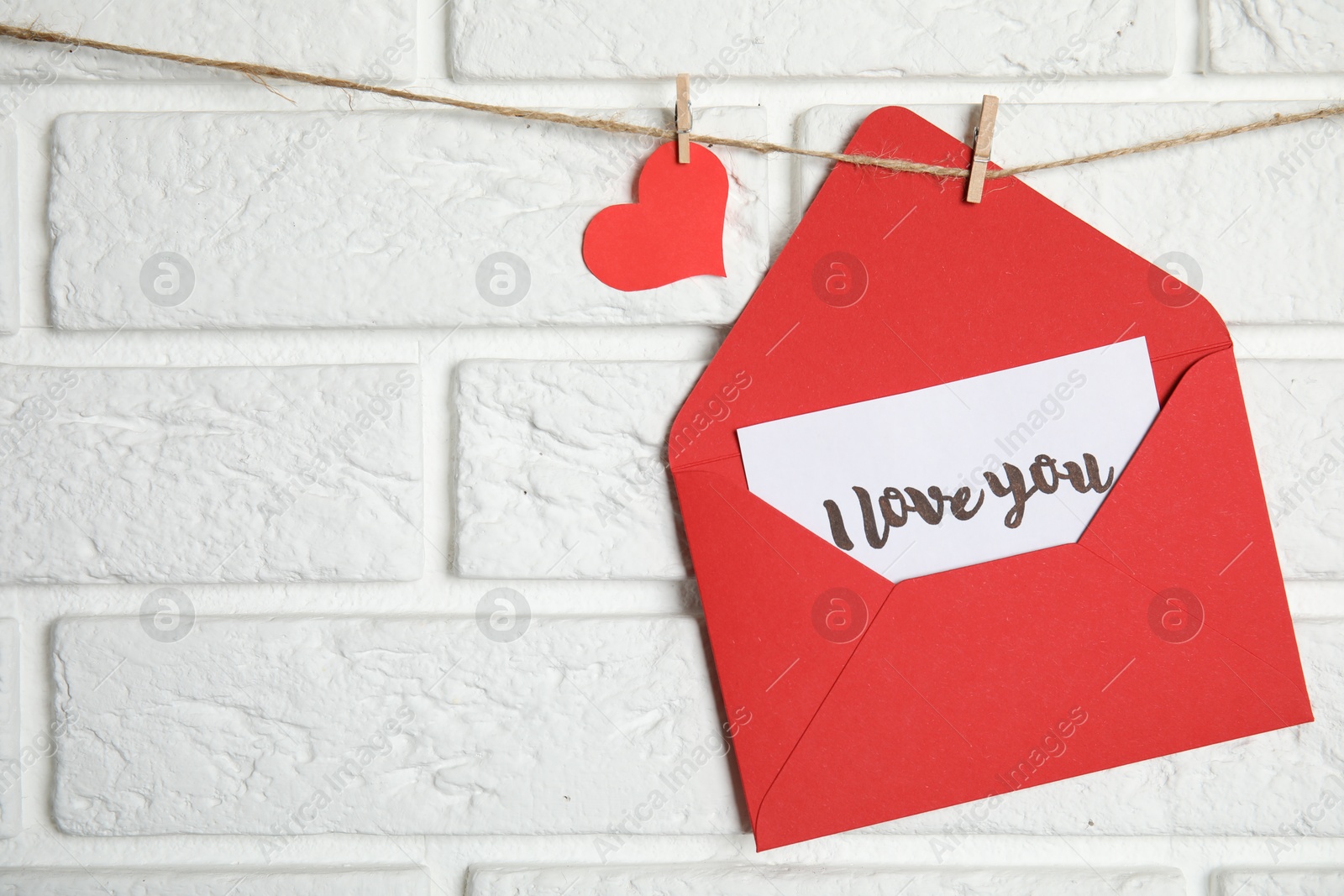 Photo of Envelope with I Love You card hanging on twine near white brick wall. Space for text