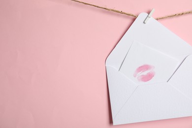 Photo of White envelope and card with lip print hanging on twine against pink background, space for text. Love letter