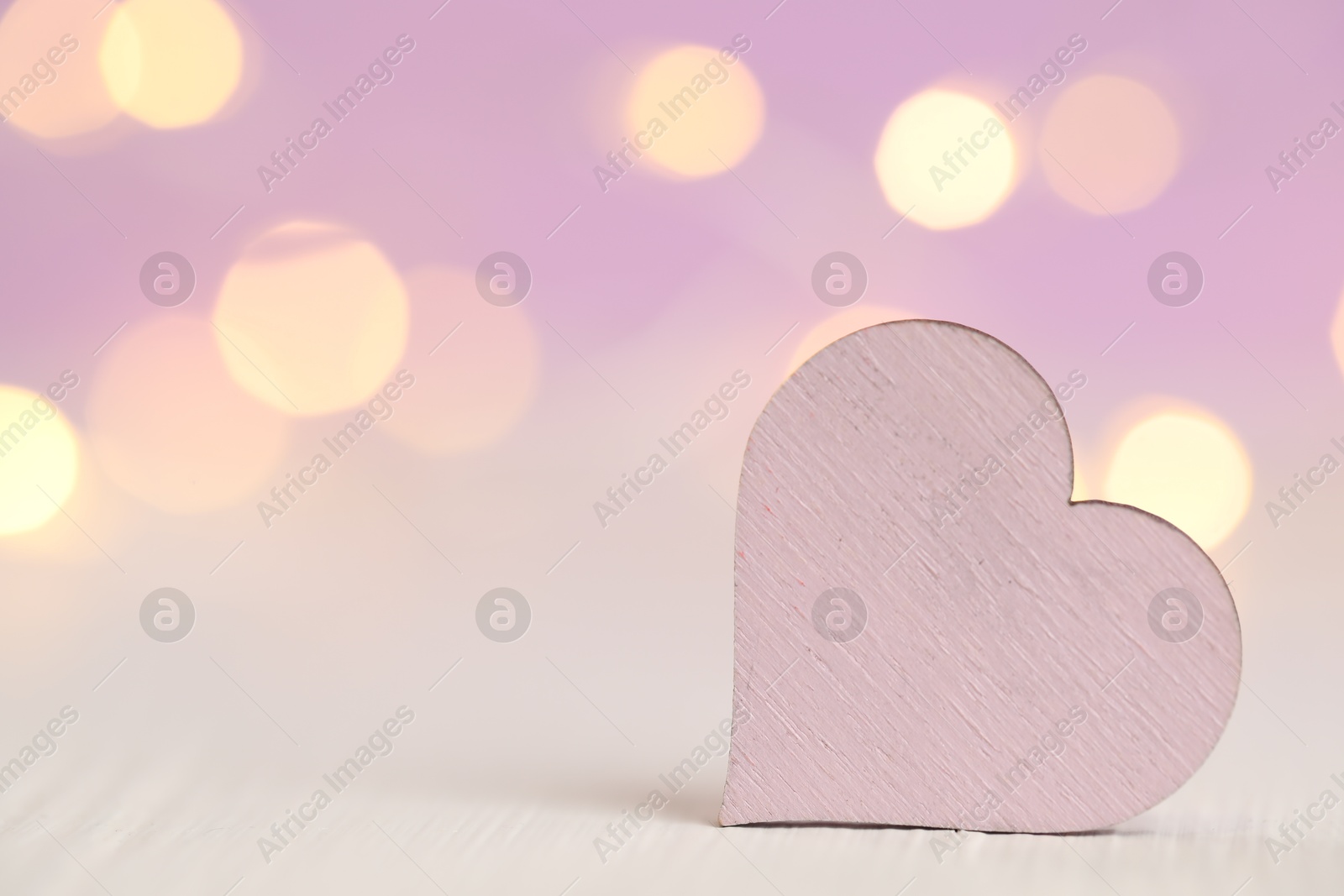 Photo of Wooden heart on white table against festive lights, space for text. St. Valentine's day