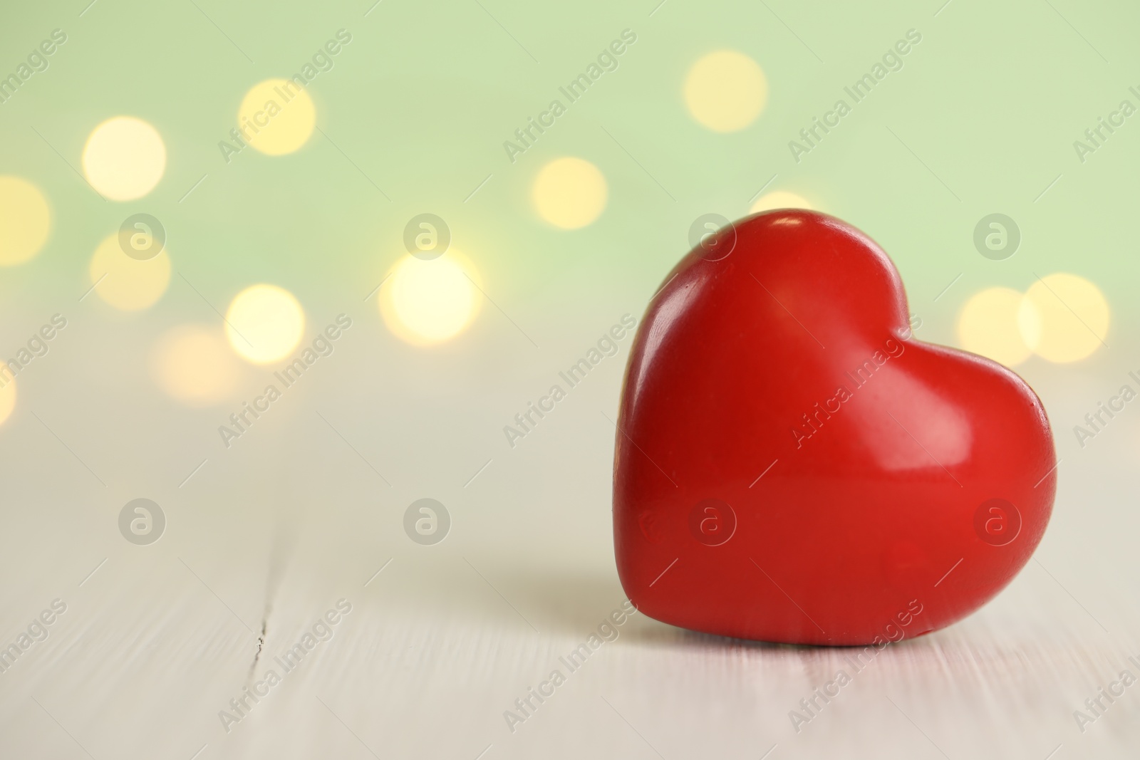 Photo of Red heart on white wooden table against festive lights, space for text. St. Valentine's day