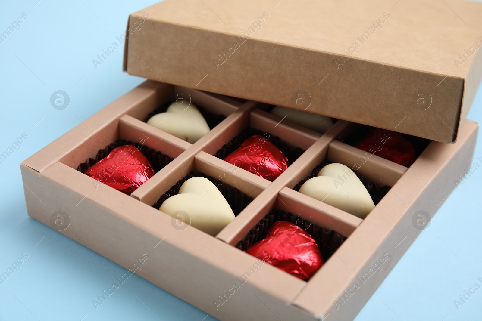 Photo of Tasty heart shaped chocolate candies on light blue background, closeup. Happy Valentine's day